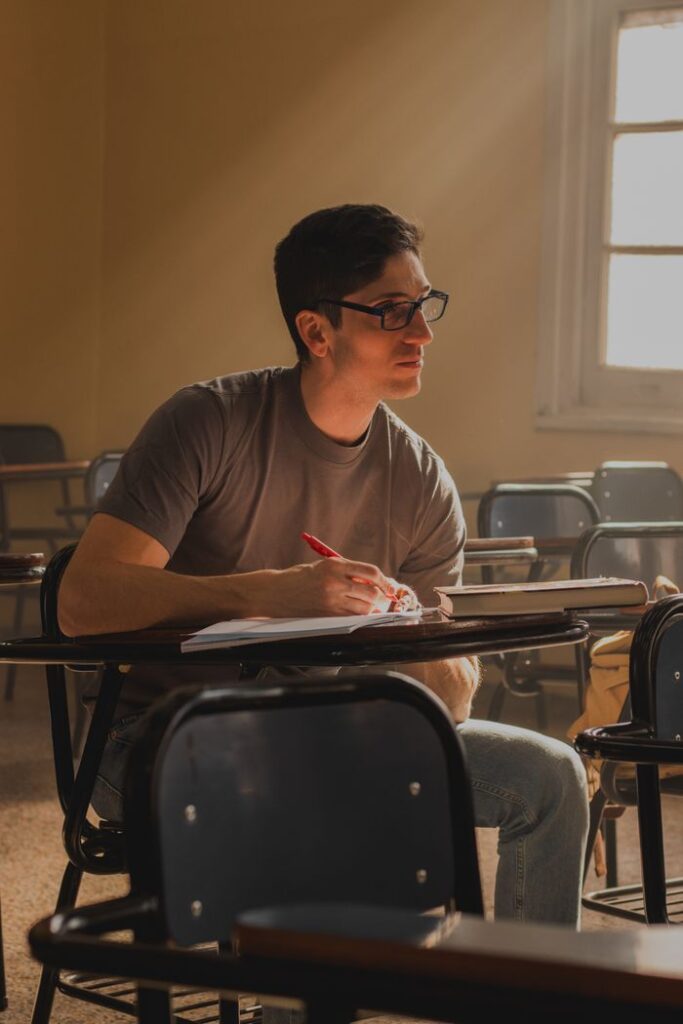 A young man attentively studies in a sunlit classroom, deep in thought.